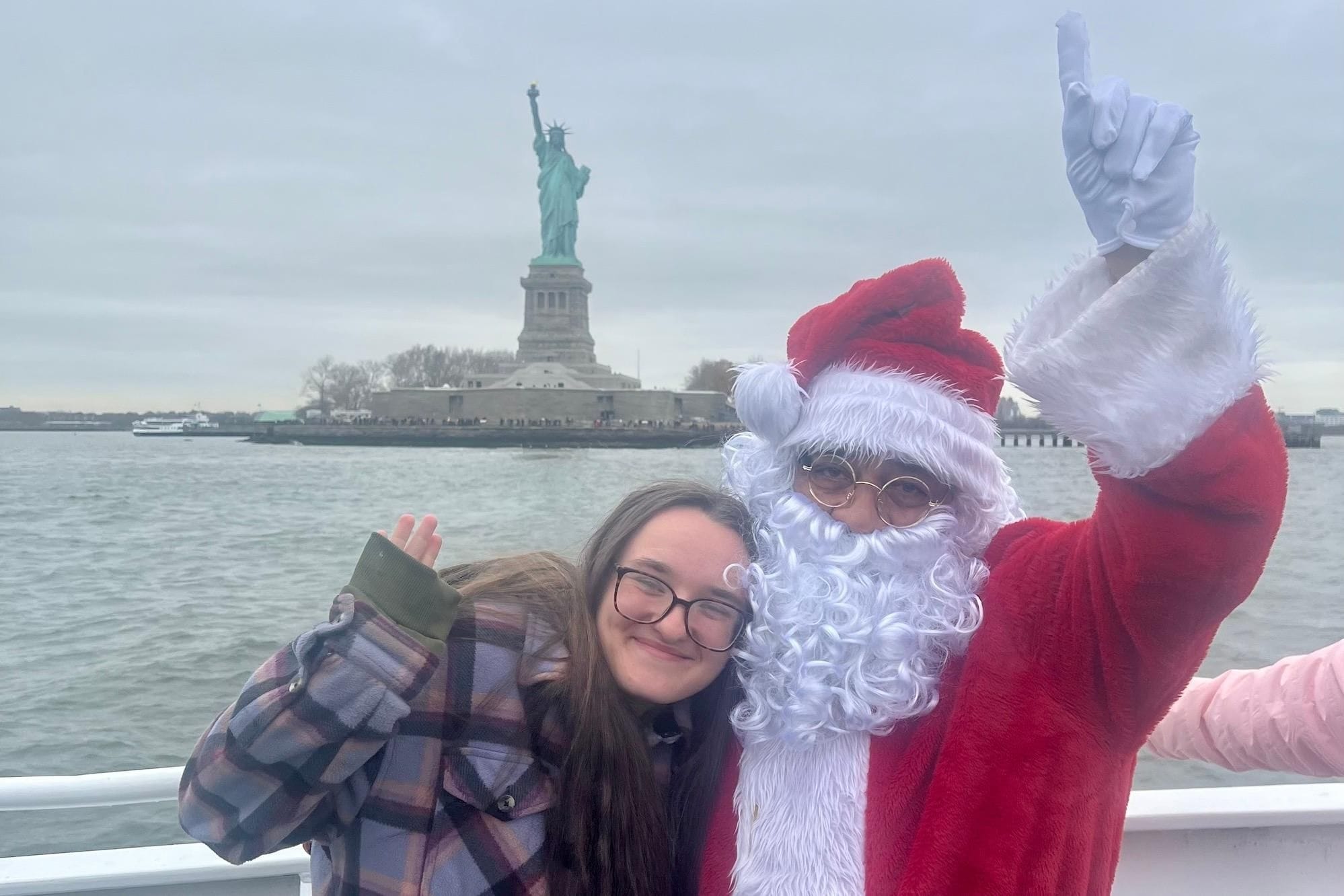 Santa and a passenger aboard a sightseeing boat with the Statue of Liberty behind them.
